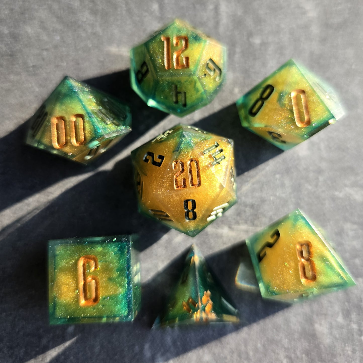 Set of green and gold polyhedral dice on a gray surface