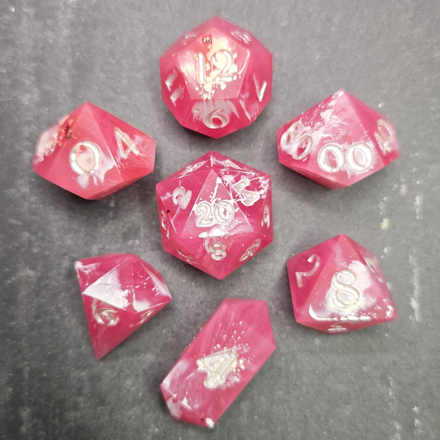 Pink and white polyhedral dice set on a gray surface