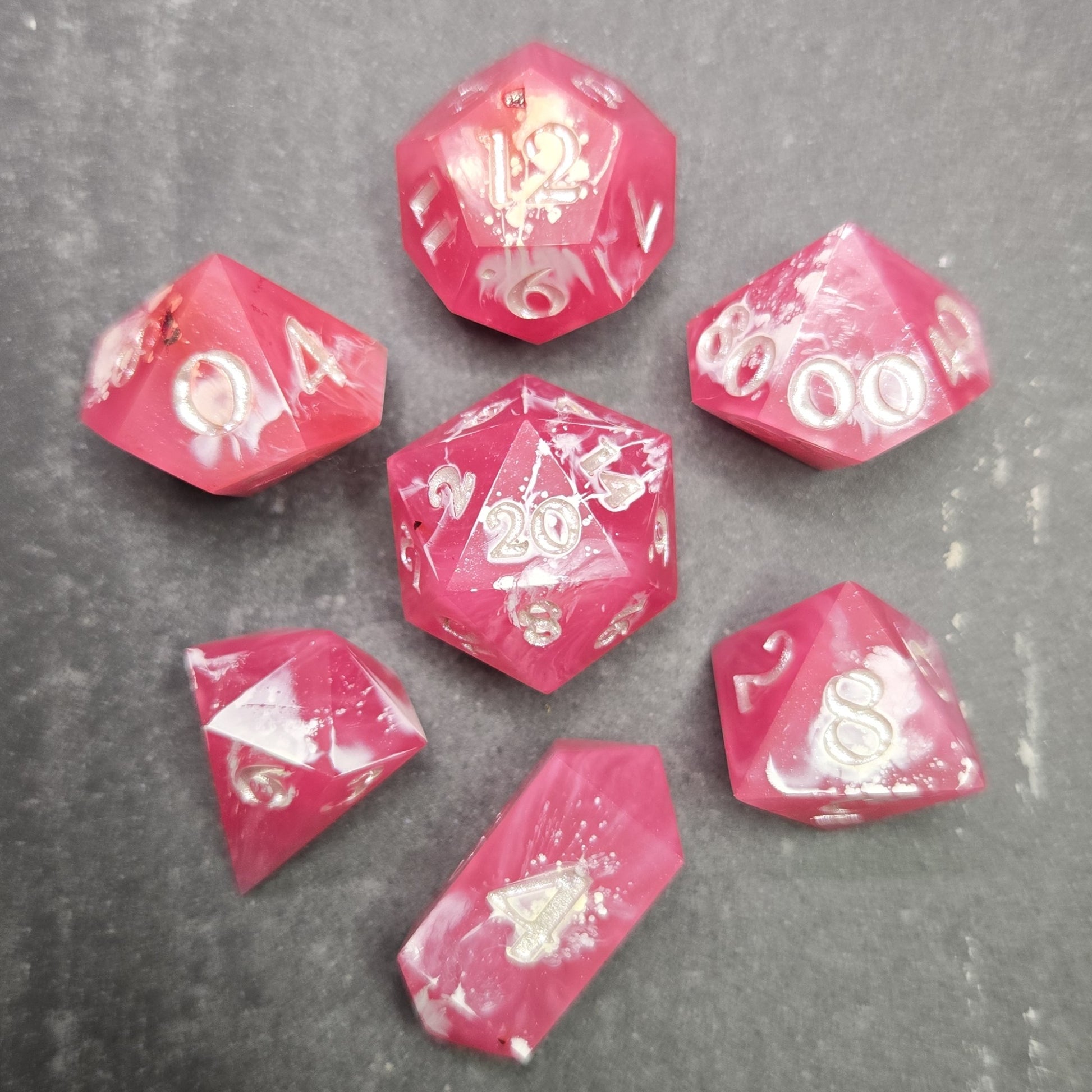 Pink and white polyhedral dice set on a gray surface